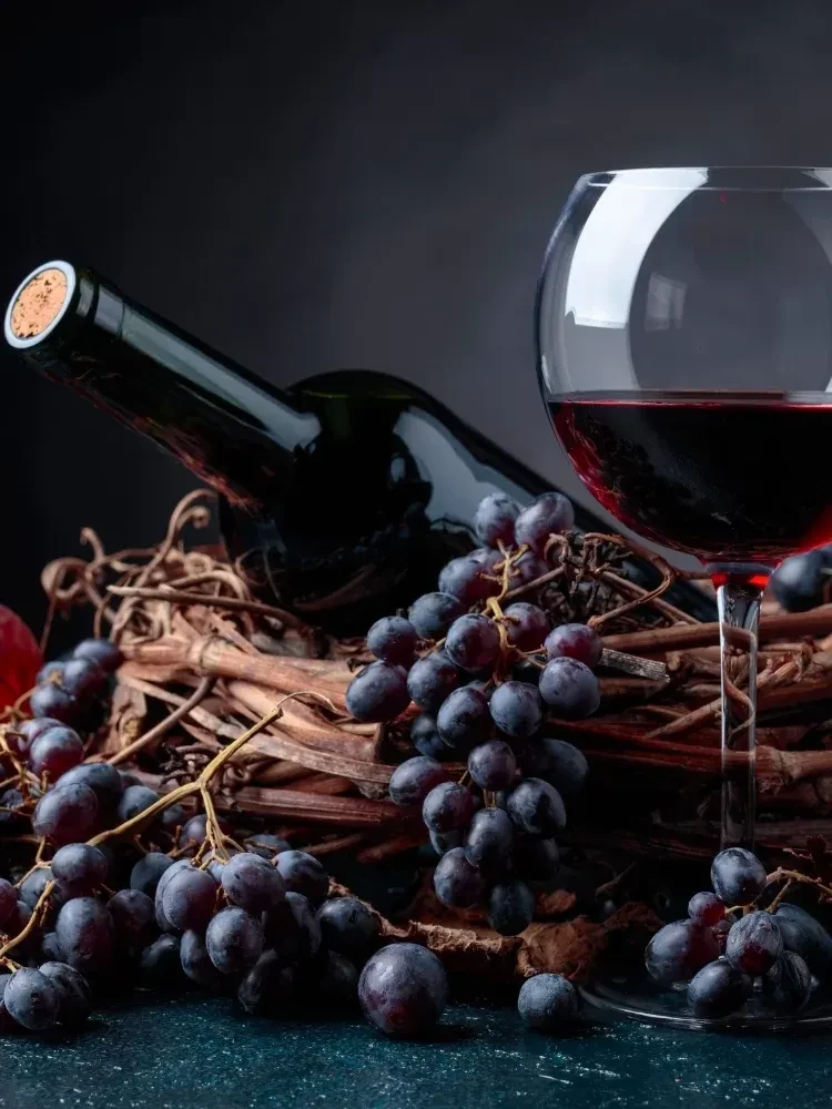 A wine bottle, glass of red wine, and grapes on twisted vines.
