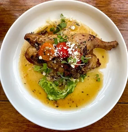 Roasted chicken with cherry tomatoes, cheese, and microgreens on a white plate.
