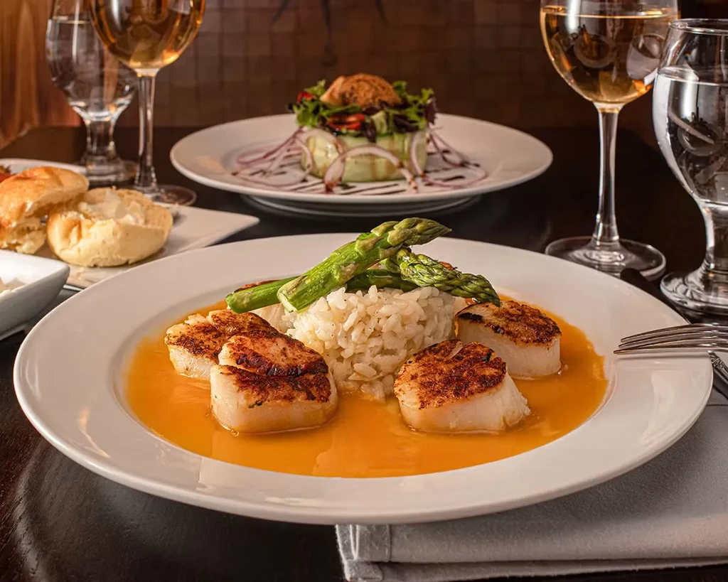 Plated seared scallops, rice, and asparagus in a restaurant setting.