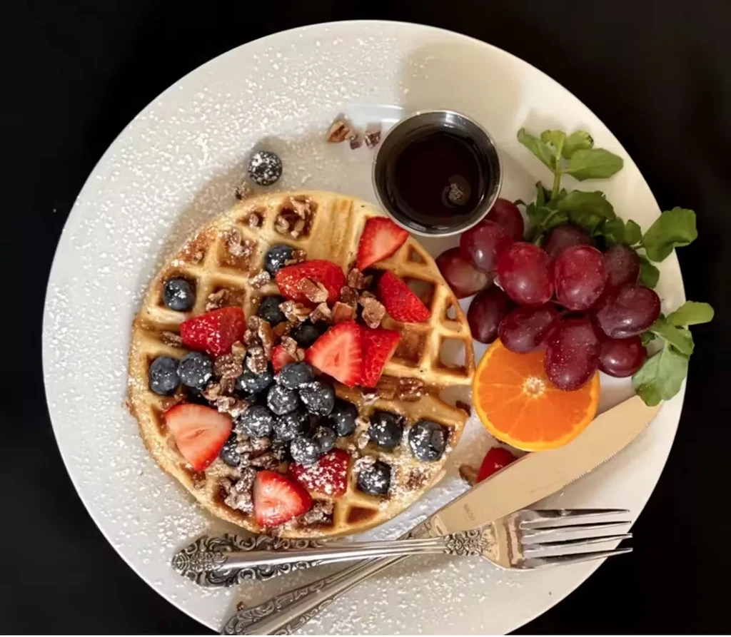 Waffle with strawberries, blueberries, pecans, syrup, grapes, and orange slice.