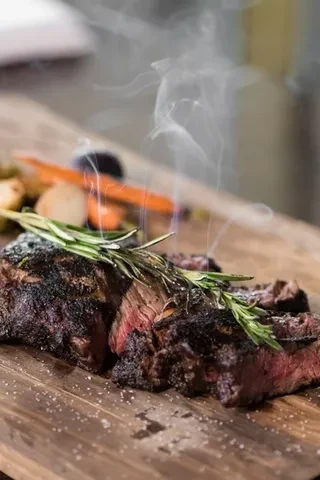 Steaming rare steak with herbs, salt, and vegetables on a cutting board.
