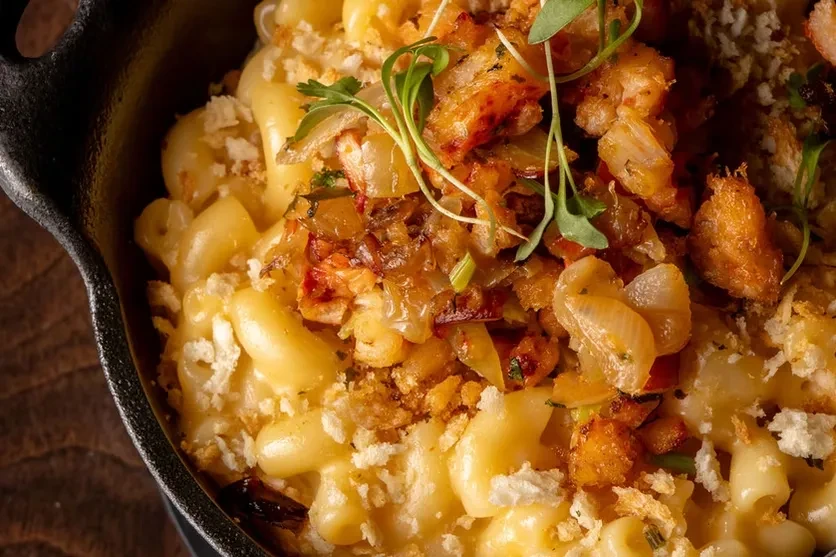 Macaroni and cheese with fried onions, shrimp, and croutons in a skillet.