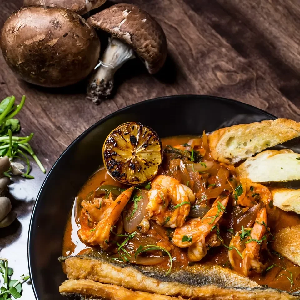 A black bowl of shrimp and fish stew with a grilled lemon.