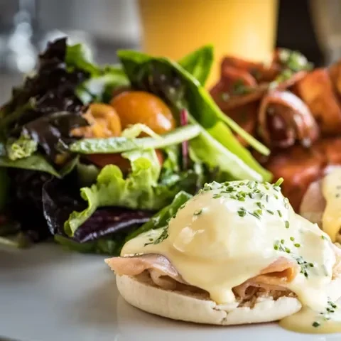 Egg Benedict, side salad, and bacon-wrapped items on a white plate.