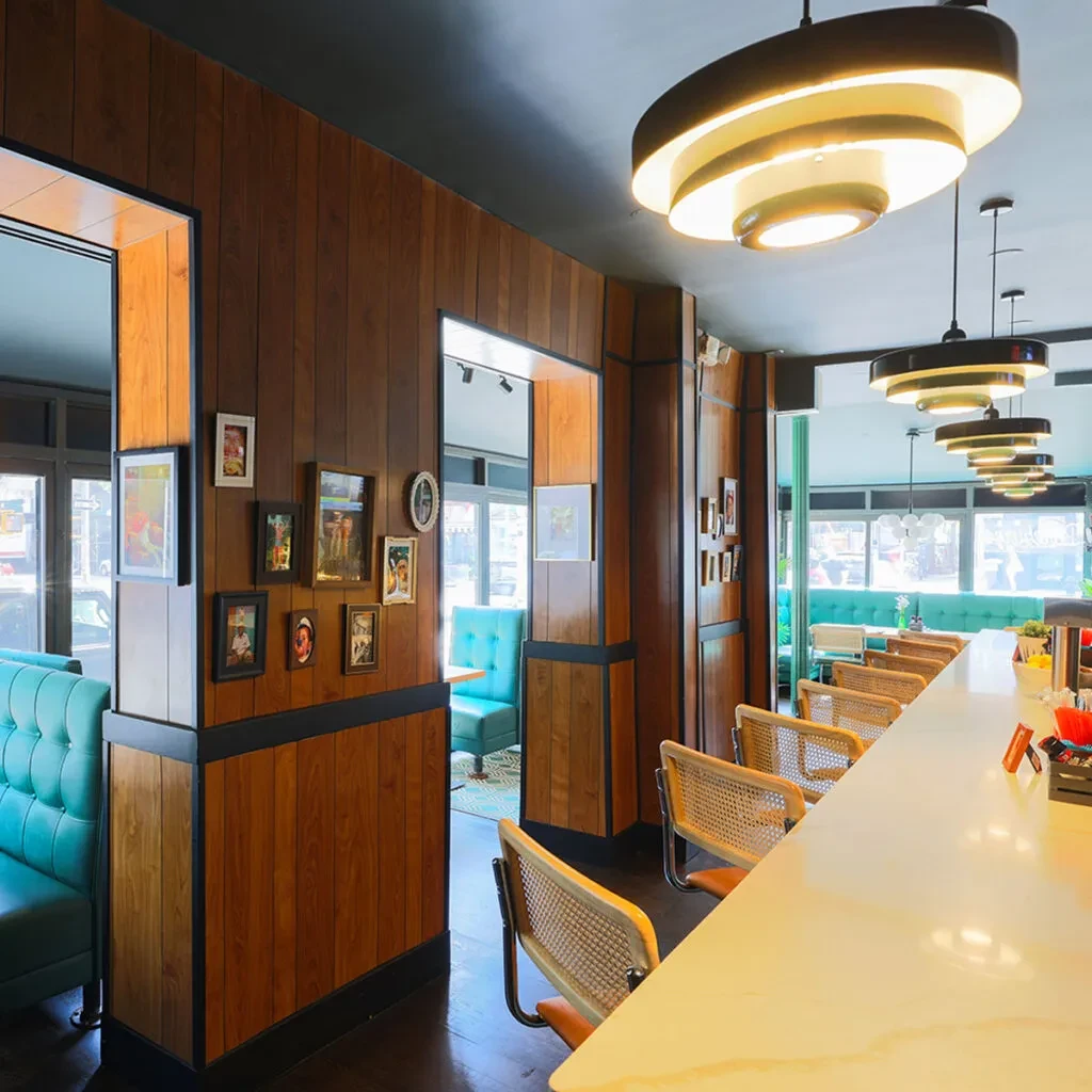 Restaurant interior with light counter, cane stools, wood-paneled wall, turquoise booths.