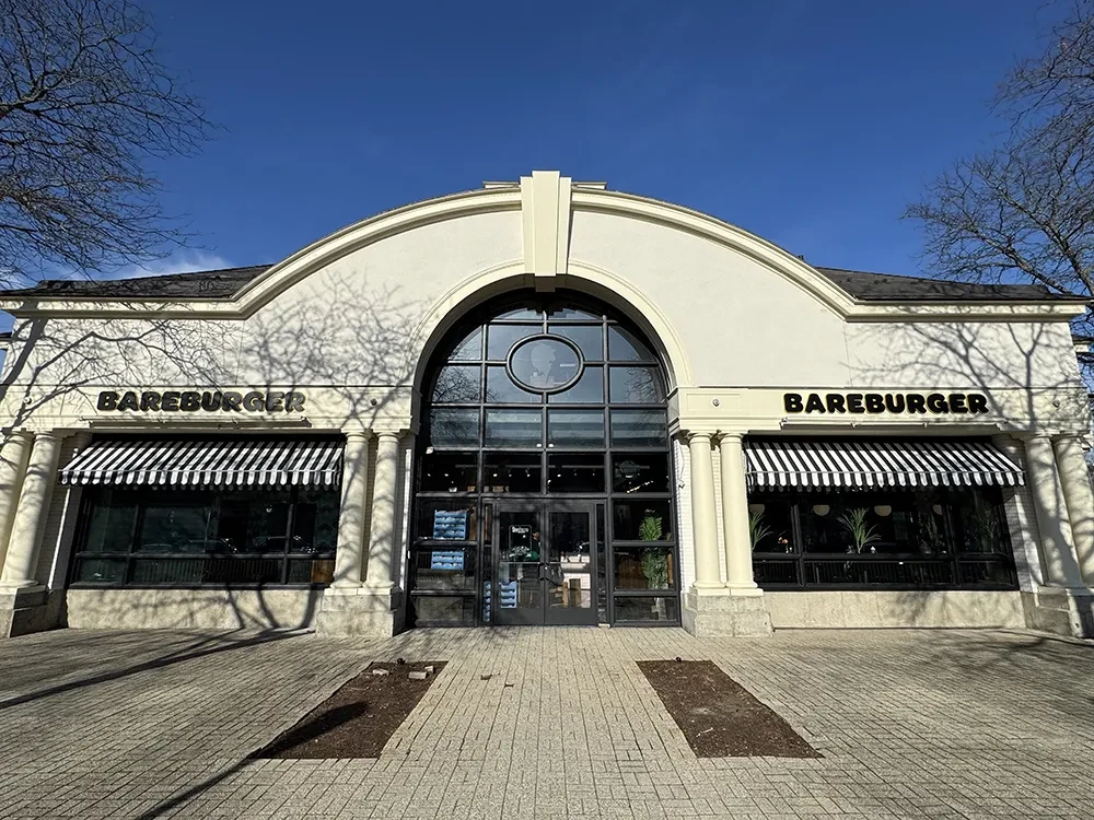 BAREBURGER restaurant exterior with cream stucco, striped awnings, and tree shadows.