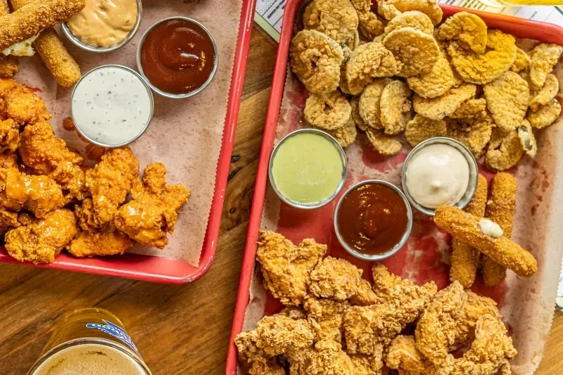 Two red trays of fried foods with dipping sauces and beer.