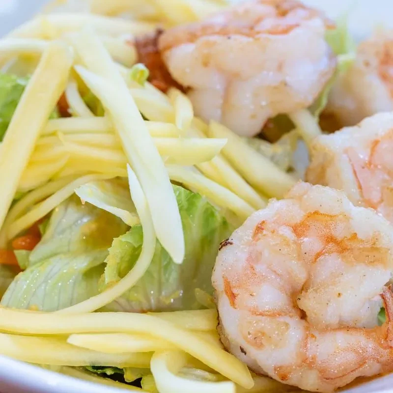 Closeup of a mango salad with grilled shrimp and lettuce.