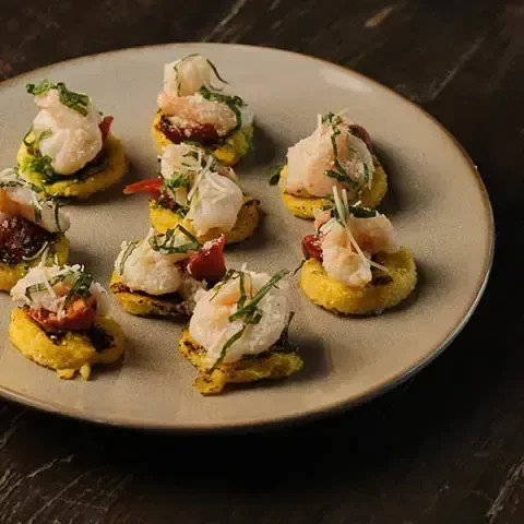 A plate of nine appetizers with shrimp, cheese, and herbs on polenta bites.
