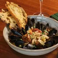 A white bowl of mussels and broth with two slices of bread.