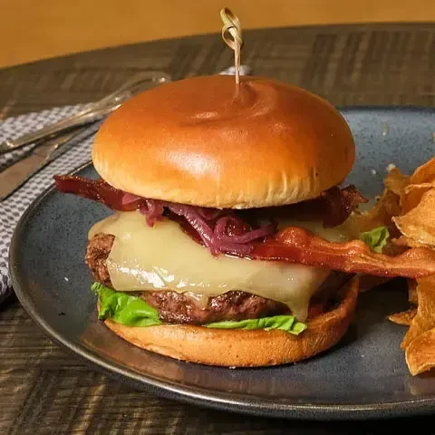 A gourmet burger with cheese, bacon, and caramelized onions on a plate.