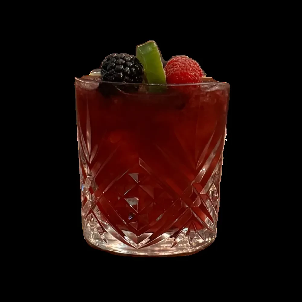 A red cocktail in a cut glass, garnished with berries and lime.