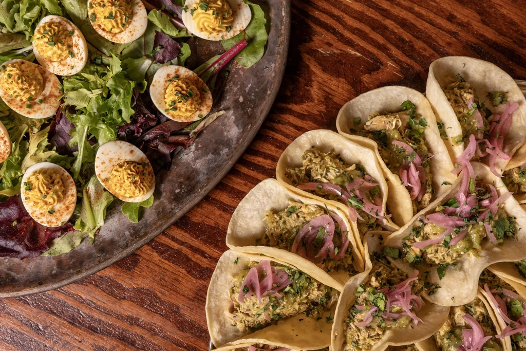 Deviled eggs with paprika on lettuce, next to chicken tacos with pickled onions.