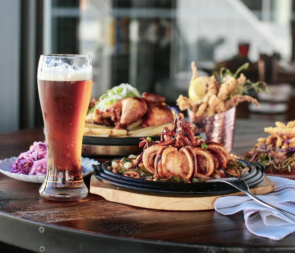 A glass of beer and multiple plates of food on a table.
