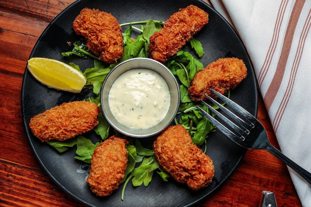 Six breaded fried oysters with tartar sauce, lemon wedge, and arugula.