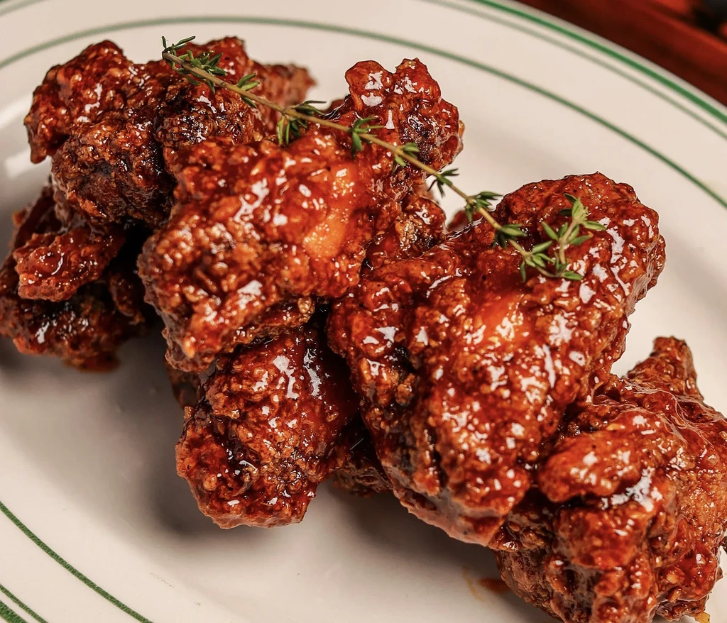 Several glazed, crispy chicken wings with fresh thyme sprigs on a white plate.