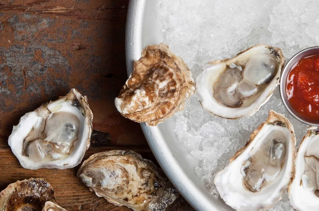 Raw oysters on ice with a side of red sauce.
