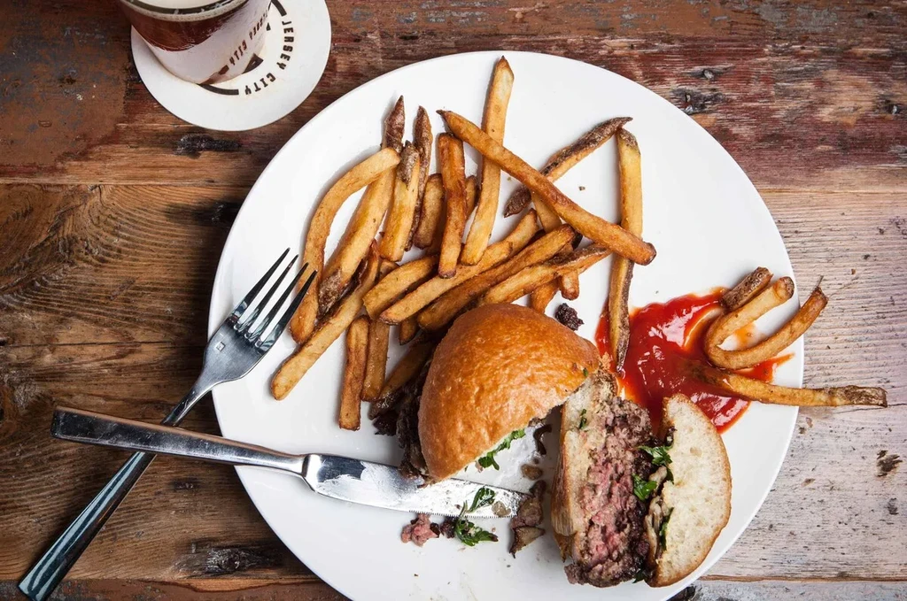 Overhead shot of a cut burger, fries, and ketchup on a white plate.