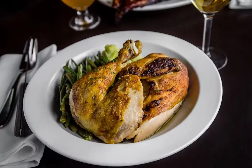 Half roasted chicken with green beans and mashed potatoes on a white plate.