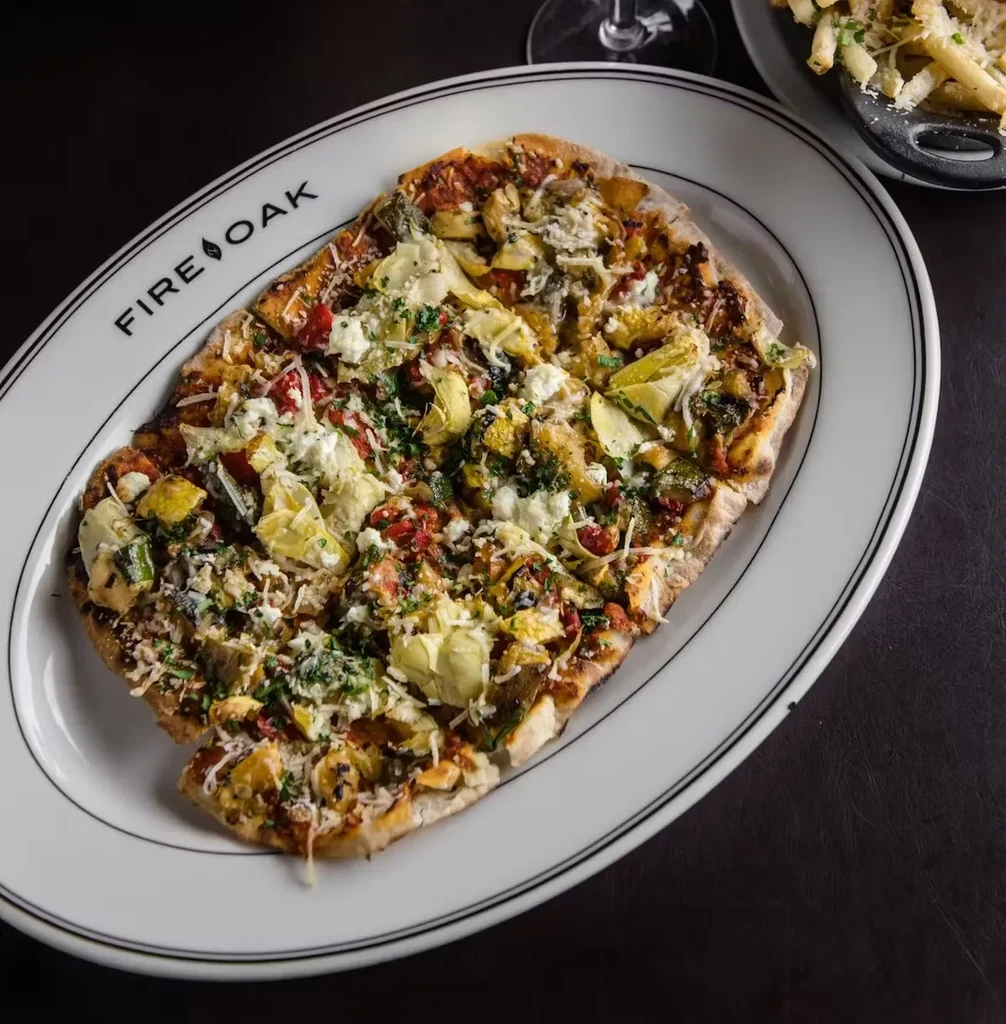 An oval white platter with a flatbread pizza topped with artichokes and feta.