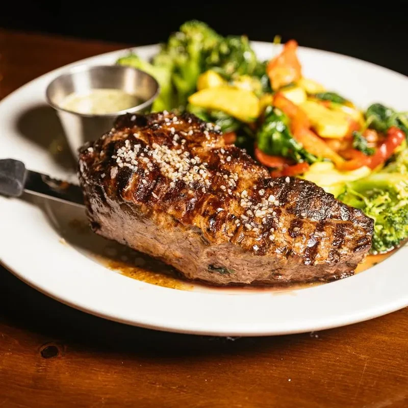 Grilled steak with salt, broccoli, and mixed vegetables on a white plate.