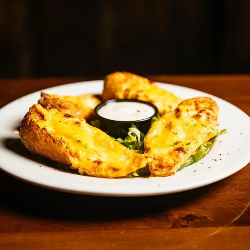 Four cheesy breadsticks with dipping sauce on a white plate.