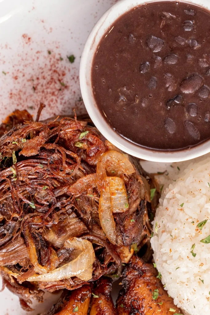 A plate of shredded beef with onions, rice, beans, and plantains.