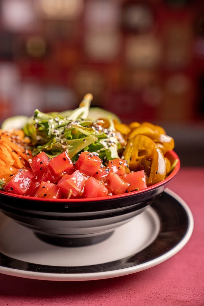 A poke bowl with tuna, lettuce, carrots, and peppers in a red bowl.