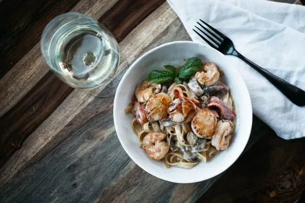 Plated seafood pasta with scallops, shrimp, basil, and wine on wood.
