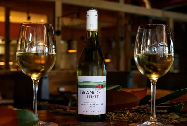 Brancott Estate Sauvignon Blanc bottle with two glasses on dark wood.
