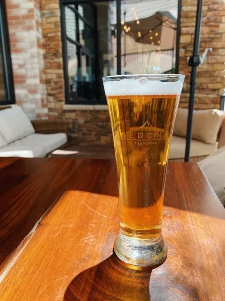 Tall glass of amber beer from Sedona Taphouse on a sunny patio.
