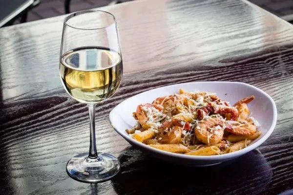 Close-up of white wine and shrimp pasta on a dark wooden table.
