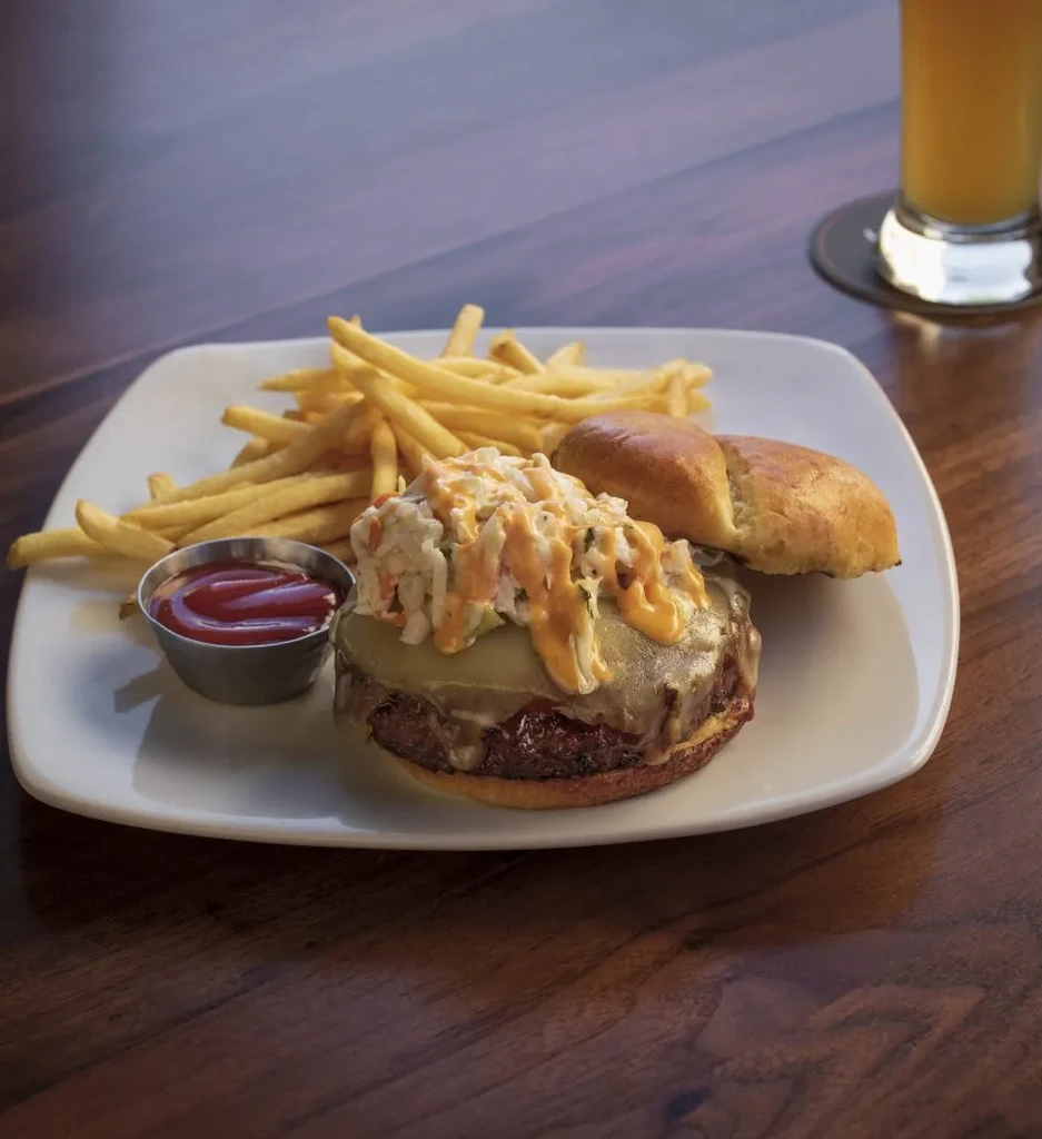 Close-up of a thick burger, golden fries, and ketchup on a plate.
