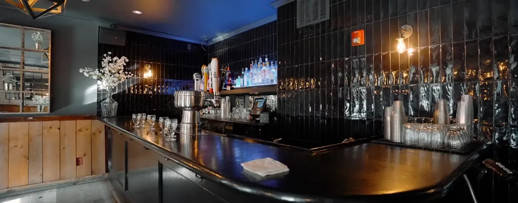 A bar with a dark countertop and black tiled wall.