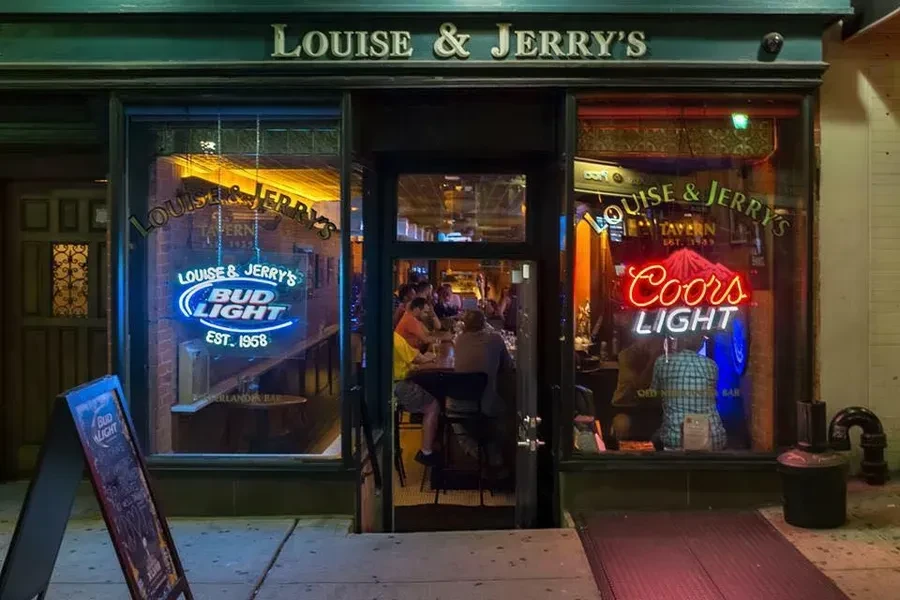 Exterior of Louise & Jerry's Bar at night, with neon beer signs.