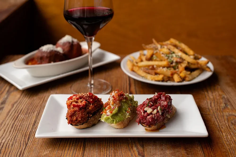 Appetizers of bruschetta, meatballs, and fries with a glass of red wine.