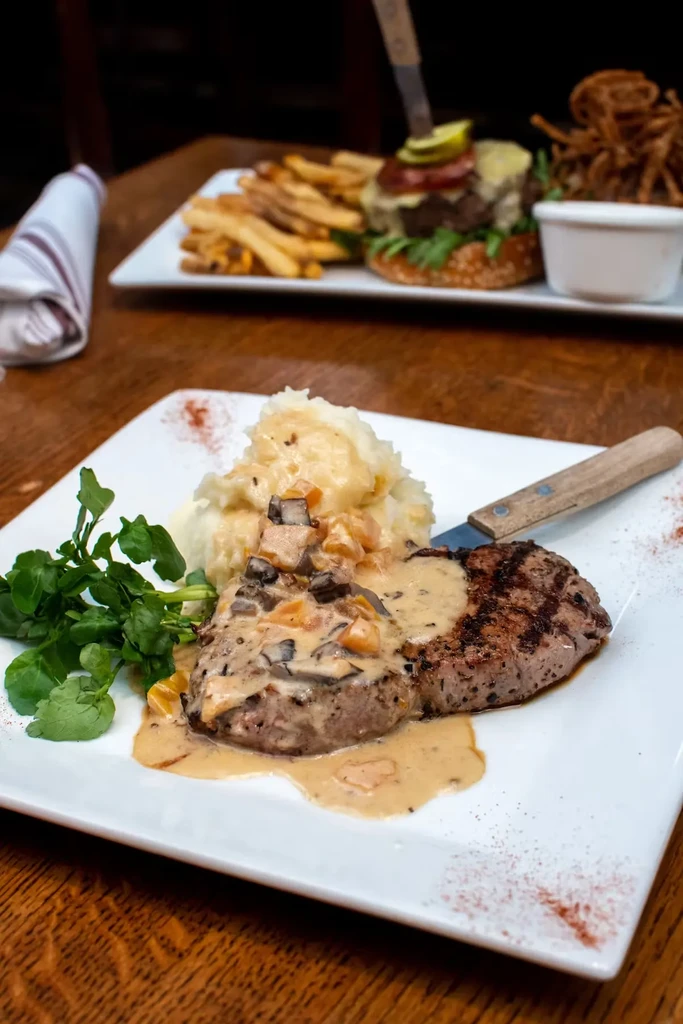 Steak with gravy and mashed potatoes, burger in the background.