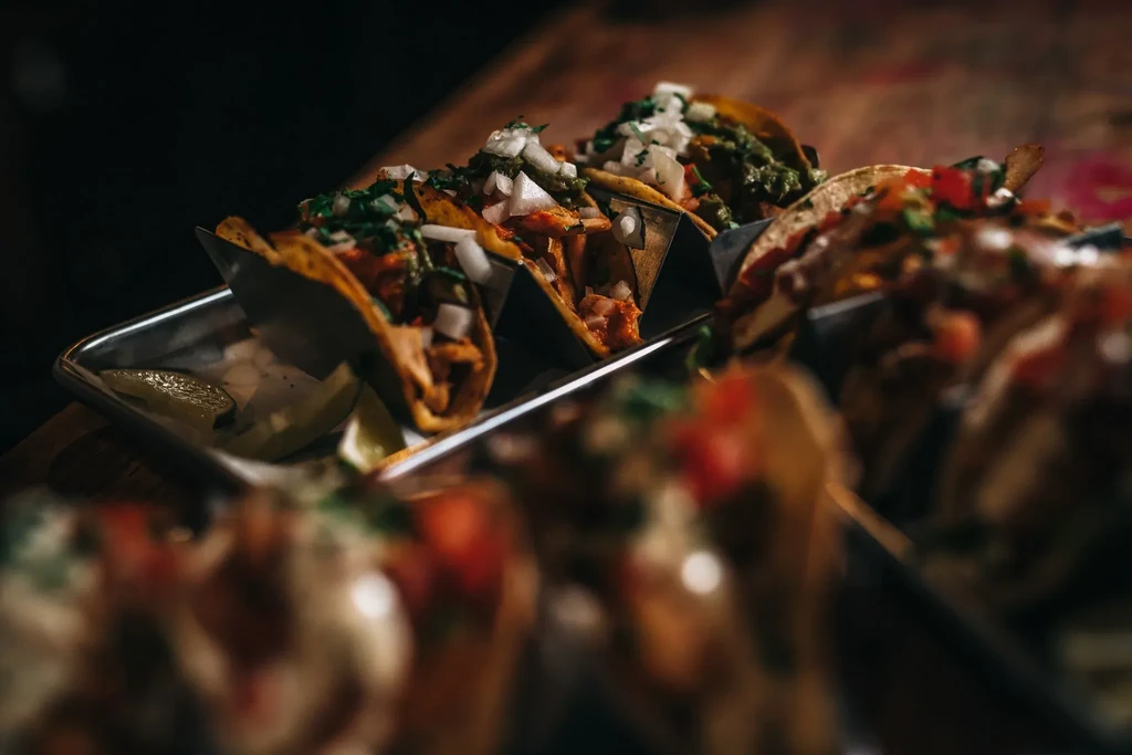 Close-up of tacos in metal stands with lime wedges on a dark background.