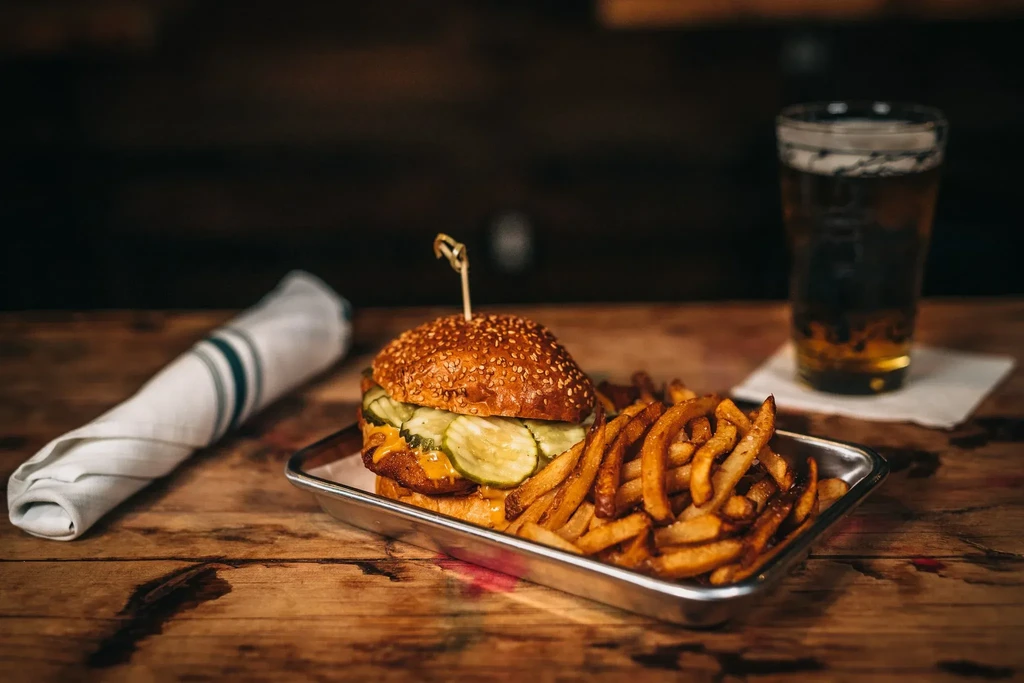 Burger, fries, and a beer on a wooden table.