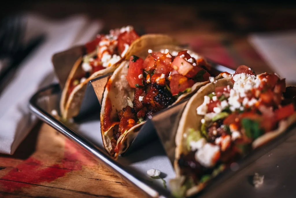 Four street tacos with meat, salsa, and cheese on a tray.