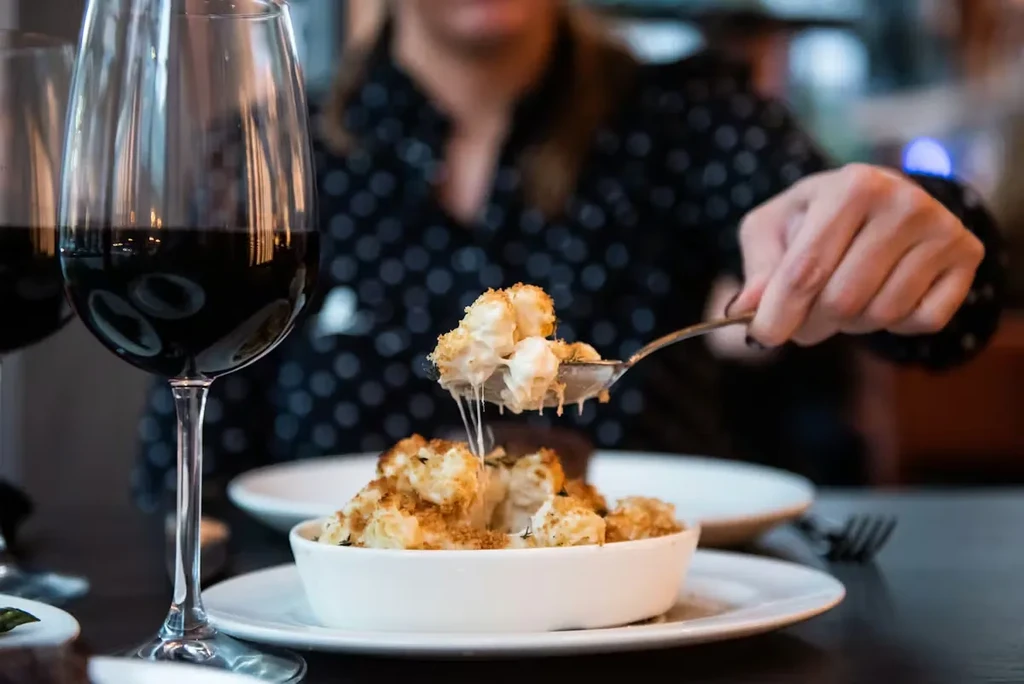 Spoon lifts cheesy mac and cheese, showing melted stretch, red wine.