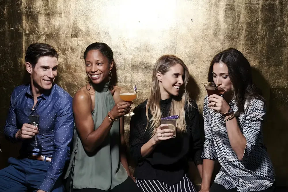 Four people smiling and drinking cocktails at a stylish bar.