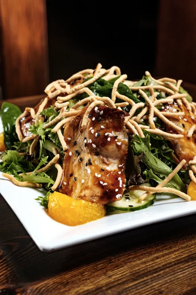 Gourmet salmon and greens with Asian noodles and orange slices.