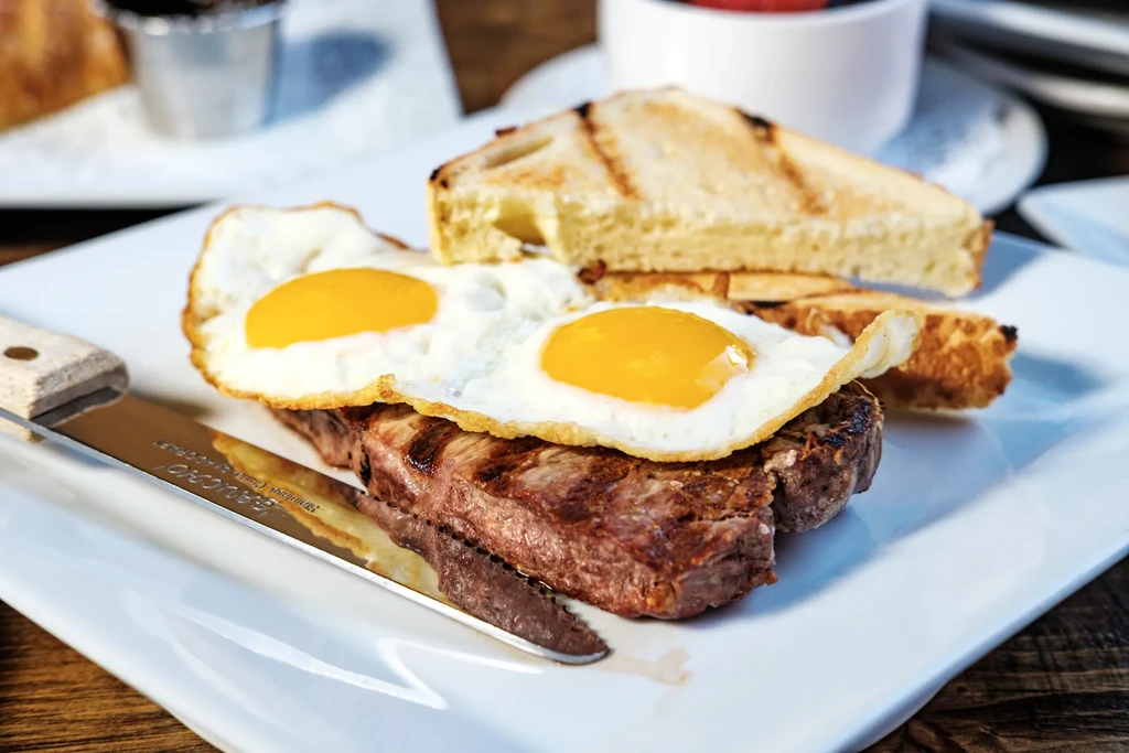 Steak and eggs breakfast with toast on a white plate.