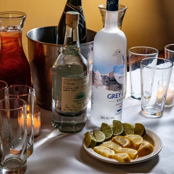 A tabletop with liquor bottles, glasses, and sliced lemons and limes.