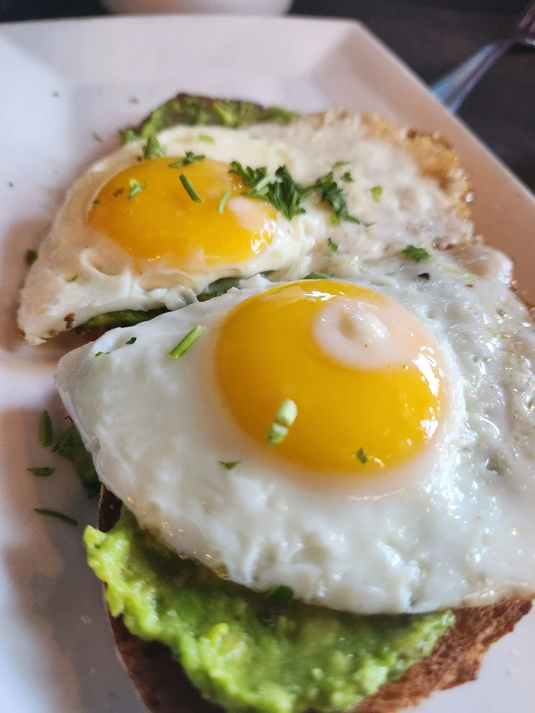 Two fried eggs with runny yolks on avocado toast, garnished with herbs.