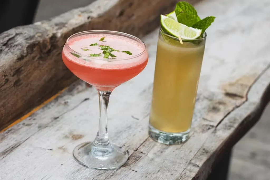 Two cocktails, one red and one yellow, on a rustic wooden table.