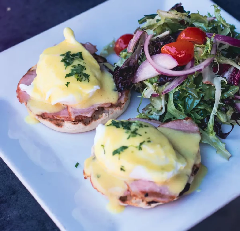 Two Eggs Benedict with side salad on a white plate.