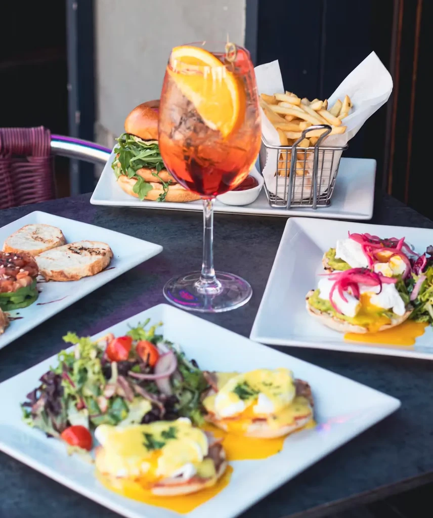 An Aperol Spritz, burgers, fries, and eggs benedict on a table.