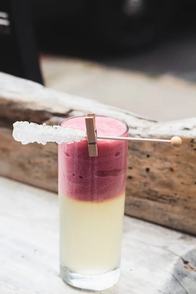 A tall glass of layered white and red drink with rock candy.